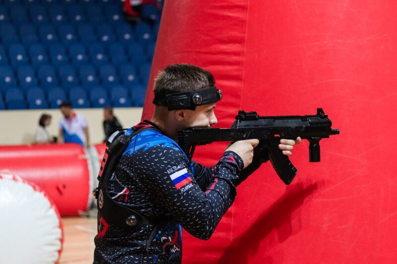 Игрок LASERWAR целится из-за красного надувного препятствия.